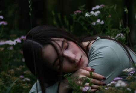 Vertical Gardens - Young female with dark hair embracing herself and putting head on hands sitting on squat in grass with blooming meadow flowers in park