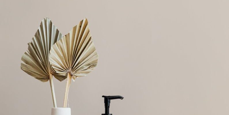 Bathroom Storage - Set of cosmetic supplies near decorative leaves in vase on marble shelf