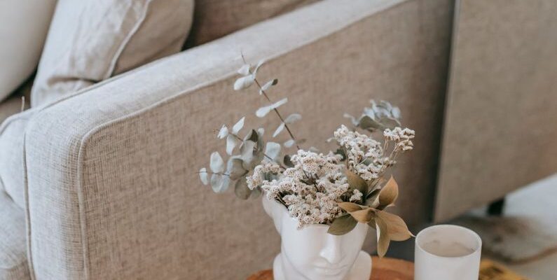 Furniture Styles - Cozy sofa with decorative cushions near stump with books and blooming flowers in vase in house room