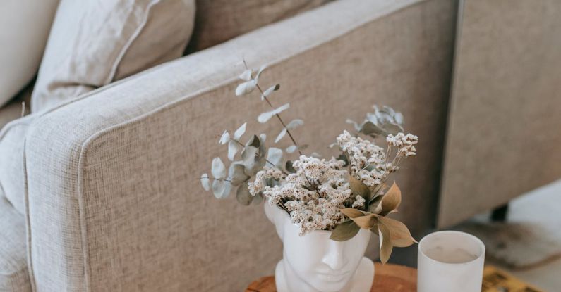 Furniture Styles - Cozy sofa with decorative cushions near stump with books and blooming flowers in vase in house room