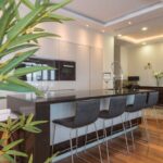 Built-In Shelves - Kitchen island with black leather chairs in spacious modern apartment with white minimalist furniture and built in appliances