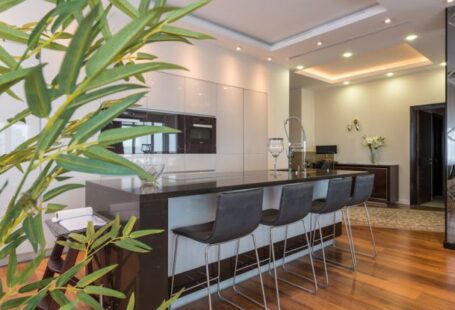 Built-In Shelves - Kitchen island with black leather chairs in spacious modern apartment with white minimalist furniture and built in appliances