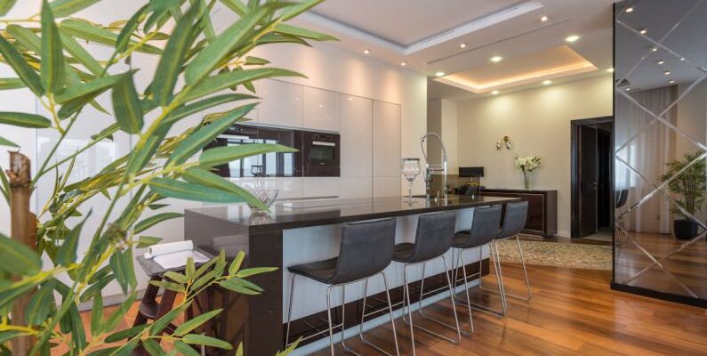 Built-In Shelves - Kitchen island with black leather chairs in spacious modern apartment with white minimalist furniture and built in appliances