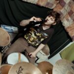 Soundproofing - From above of male musician in casual outfit sitting at drum set near wall with bottle of beer in studio