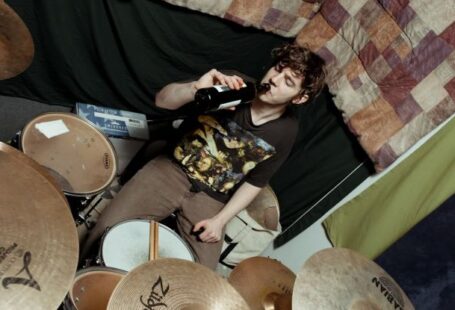 Soundproofing - From above of male musician in casual outfit sitting at drum set near wall with bottle of beer in studio