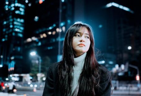 Outdoor Lighting - Brunette Girl Sitting on Bench in City Street at Night