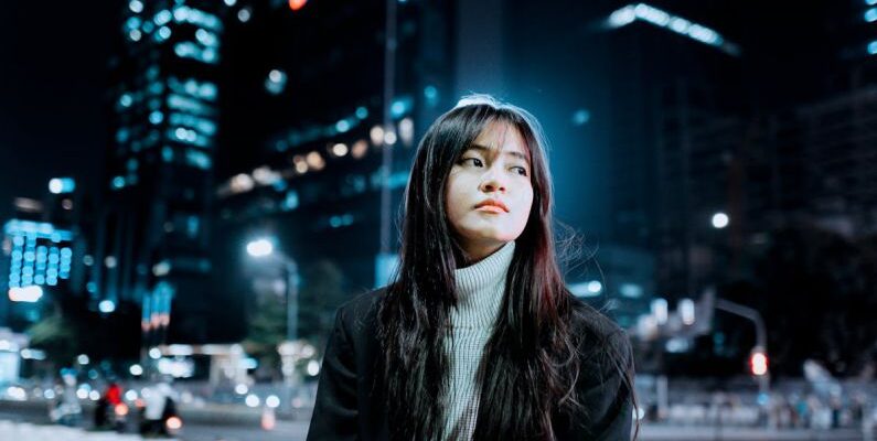 Outdoor Lighting - Brunette Girl Sitting on Bench in City Street at Night