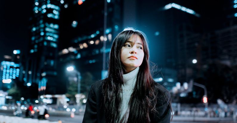 Outdoor Lighting - Brunette Girl Sitting on Bench in City Street at Night