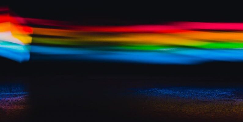Lighting Trends - Colorful abstract background with blurred glowing rainbow lights in modern dark studio with black wall and creative bright optical effect