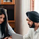 Smart Home Assistant - From above of young Indian male tutor and female student sitting at table with laptop and exercise books and doing homework during individual lesson