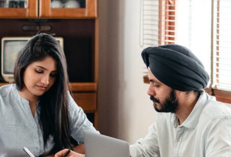 Smart Home Assistant - From above of young Indian male tutor and female student sitting at table with laptop and exercise books and doing homework during individual lesson