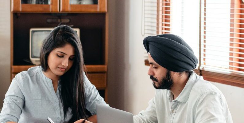 Smart Home Assistant - From above of young Indian male tutor and female student sitting at table with laptop and exercise books and doing homework during individual lesson