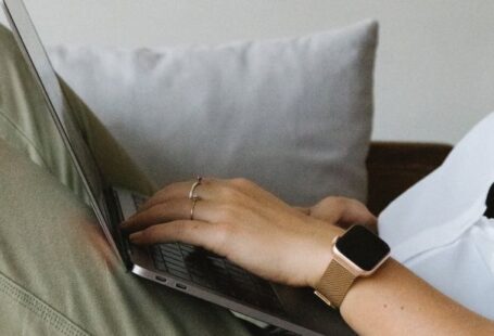 Smart Home Sensors - Side view of crop unrecognizable female freelancer in casual clothes and smartwatch lying on comfortable sofa and working remotely on laptop