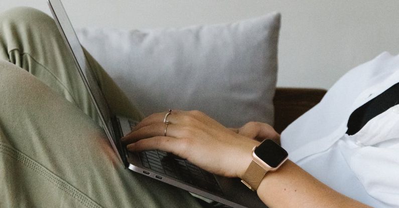 Smart Home Sensors - Side view of crop unrecognizable female freelancer in casual clothes and smartwatch lying on comfortable sofa and working remotely on laptop